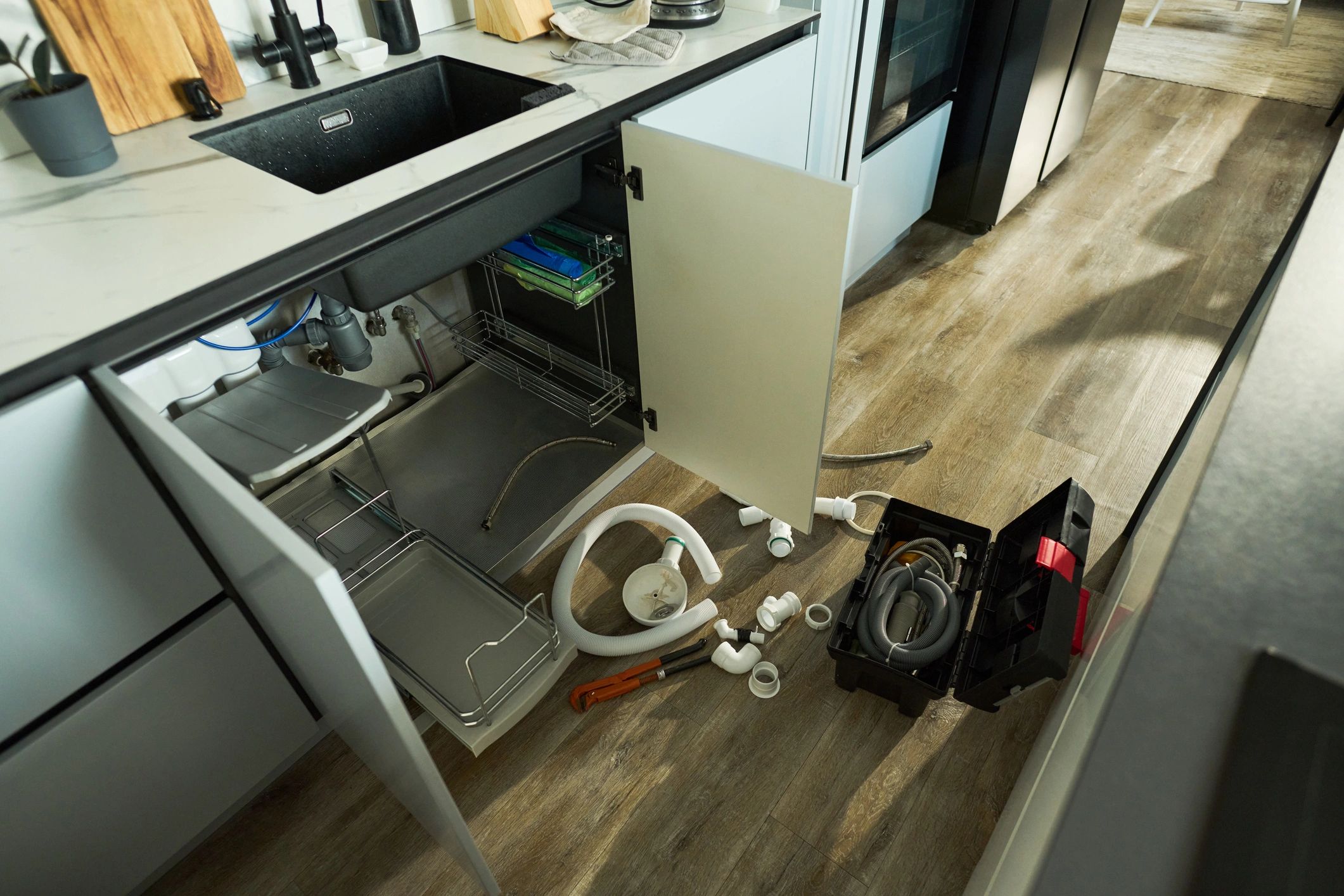 Plumbing tools and parts on the floor near a kitchen sink cabinet